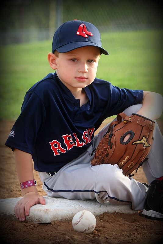 a young boy sitting on top of a baseball field wearing a catchers mitt