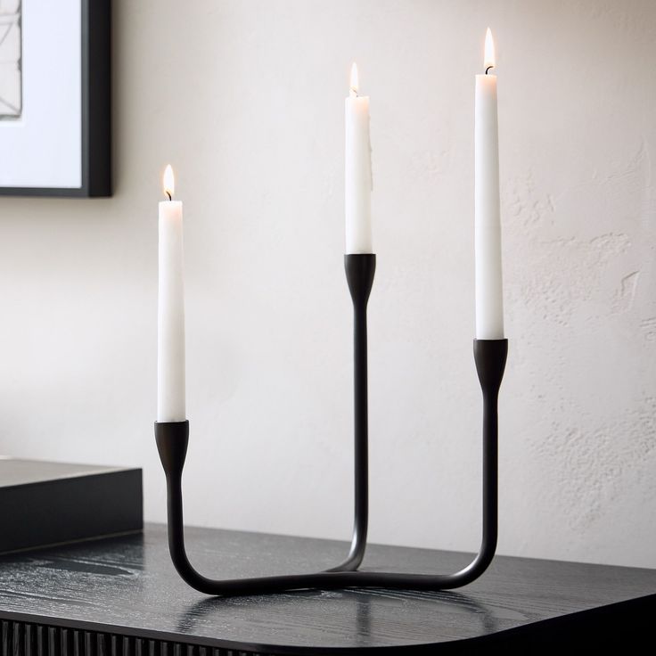 three candles are lit on a table with a black candle holder next to it and a white wall in the background