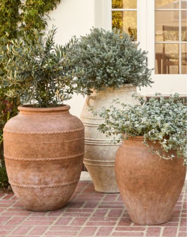 two large vases sitting on top of a brick floor next to trees and bushes