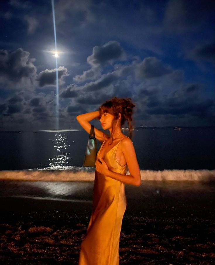 a woman is standing on the beach at night with her hair blowing in the wind