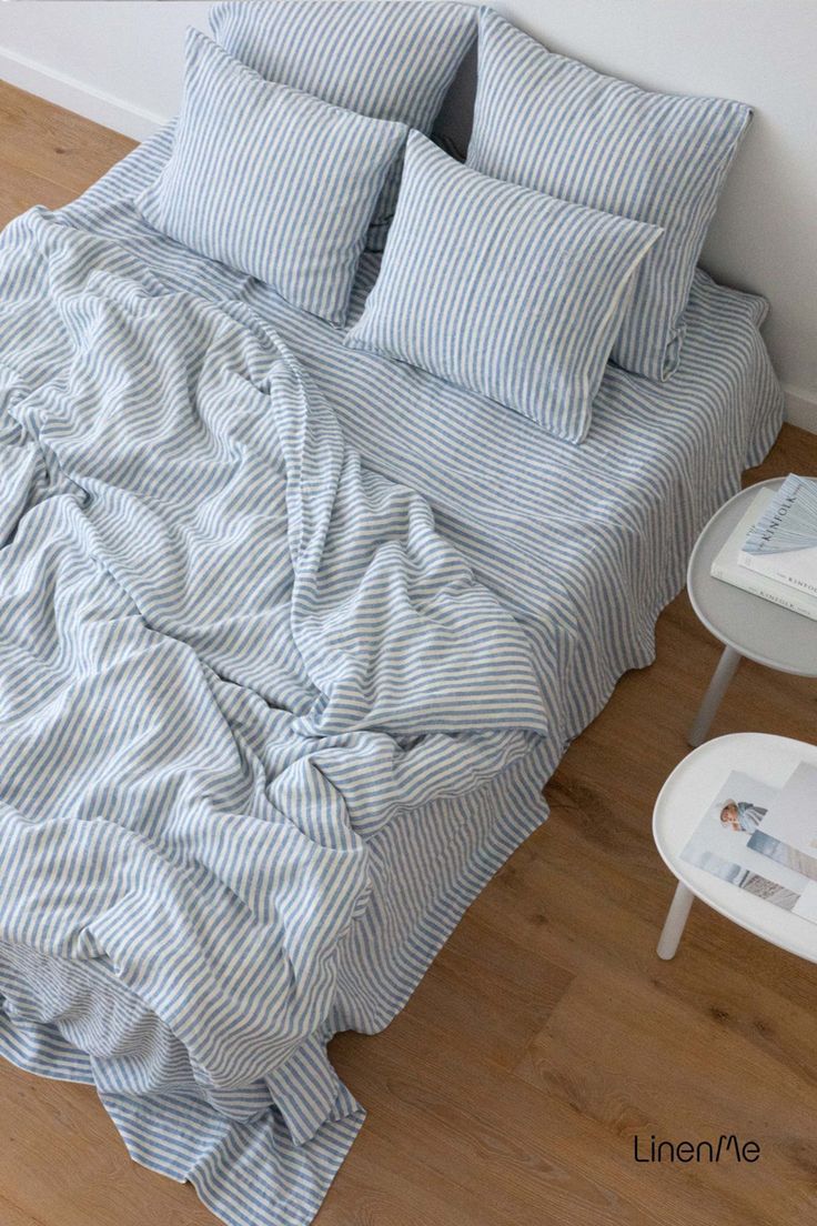 an unmade bed with blue and white striped comforter on the floor next to a small table