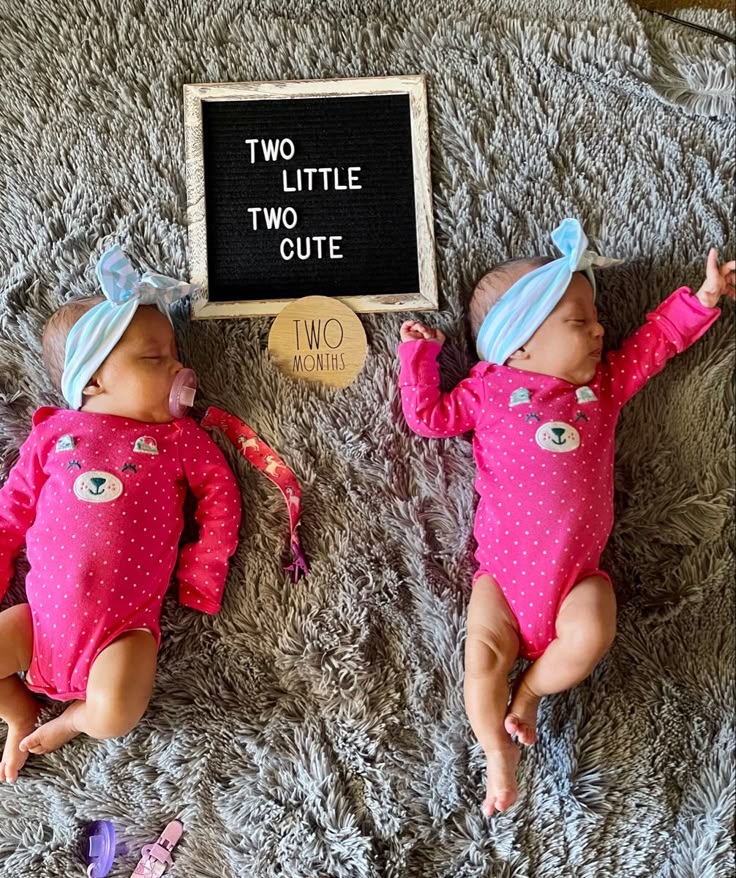 two baby dolls laying next to each other on a bed with a chalkboard that says two little cute