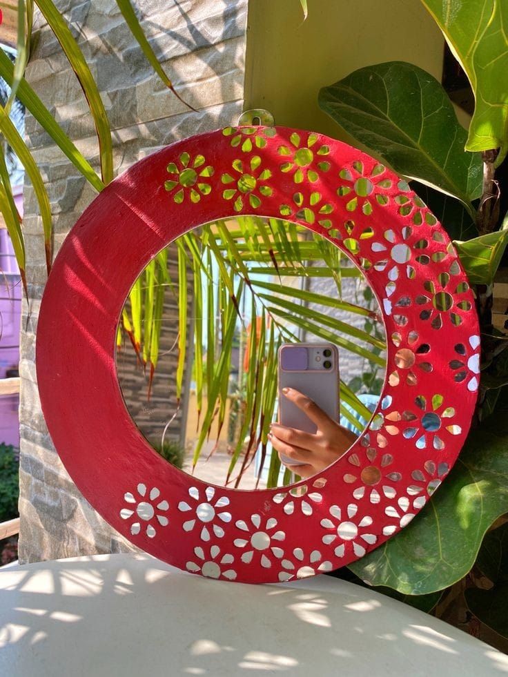 a person taking a selfie in front of a red circular mirror with flowers on it