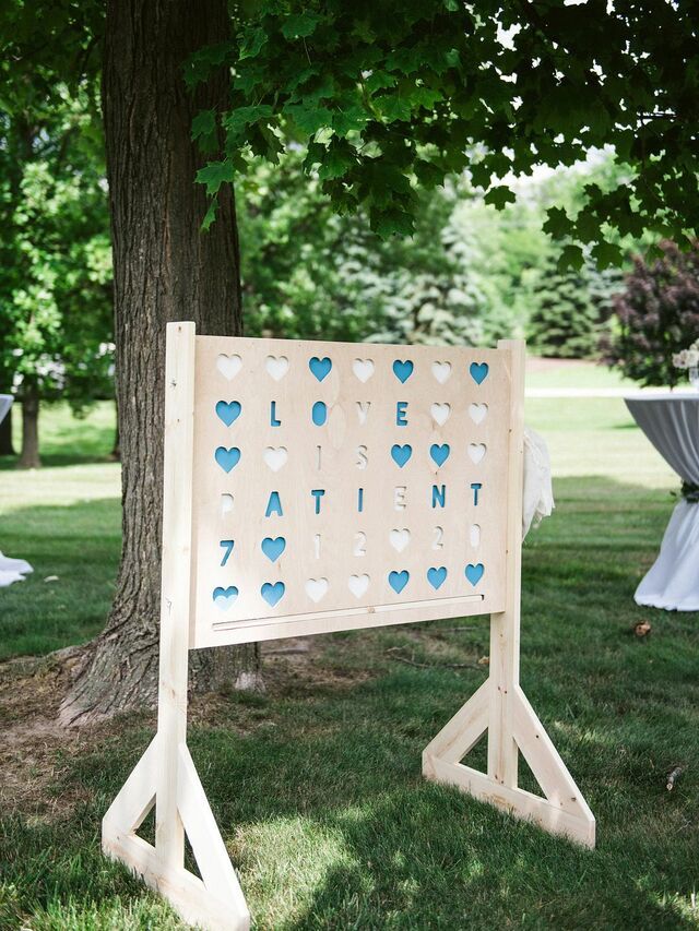 a wooden sign with hearts on it sitting in the grass next to a tree and table cloth