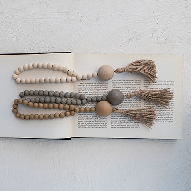 an open book with wooden beads and tassels on the pages, sitting on a white surface