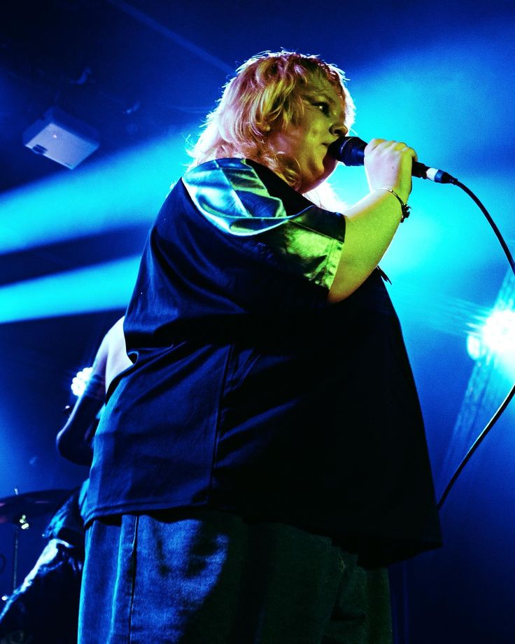 a man standing in front of a microphone on top of a stage with blue lights