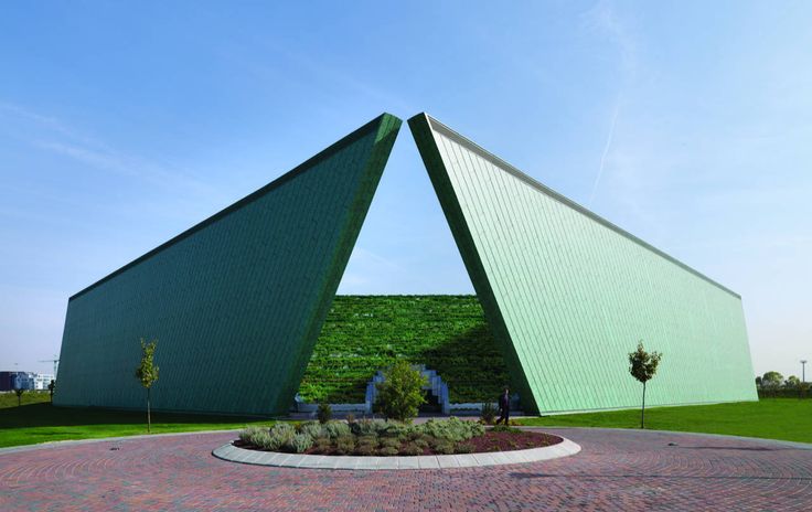 two large triangular shaped buildings in the middle of a brick circle with grass growing on top