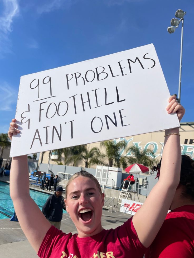 a woman holding up a sign in front of a swimming pool