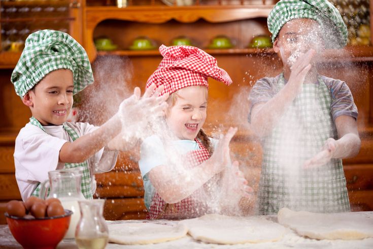 three children in aprons and hats are making dough on a table with flour coming out of them