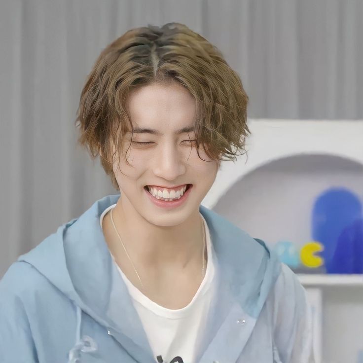 a young man smiling and wearing a blue hoodie in front of a white shelf