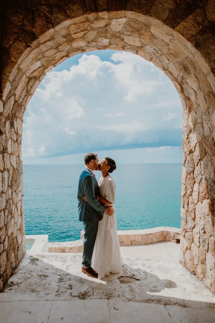 a bride and groom standing under an arch overlooking the ocean