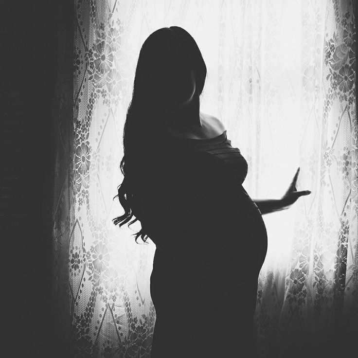 a pregnant woman standing in front of a window with her hand out to the side