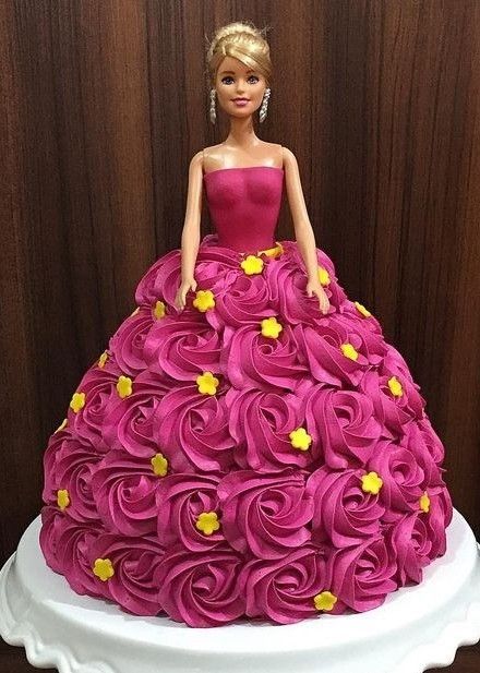 a barbie doll cake with pink and yellow flowers on it's bottom, sitting on a white plate