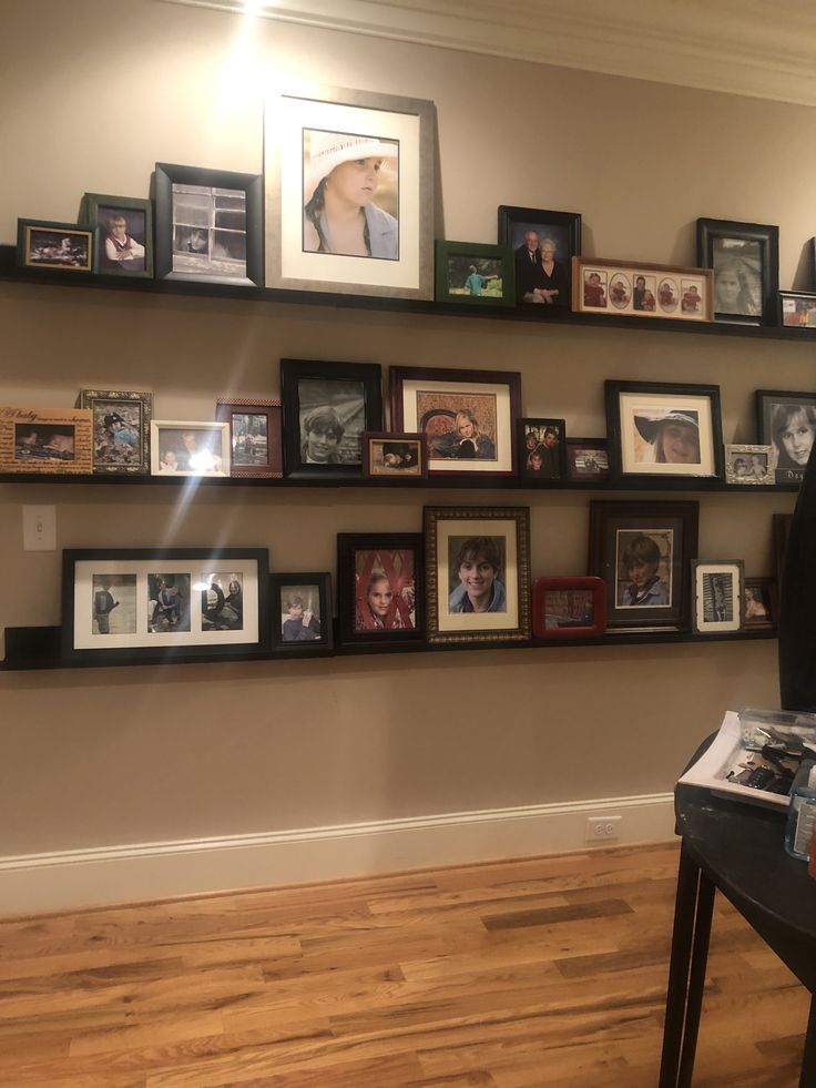 a wall filled with lots of framed pictures on top of wooden shelves next to a hard wood floor