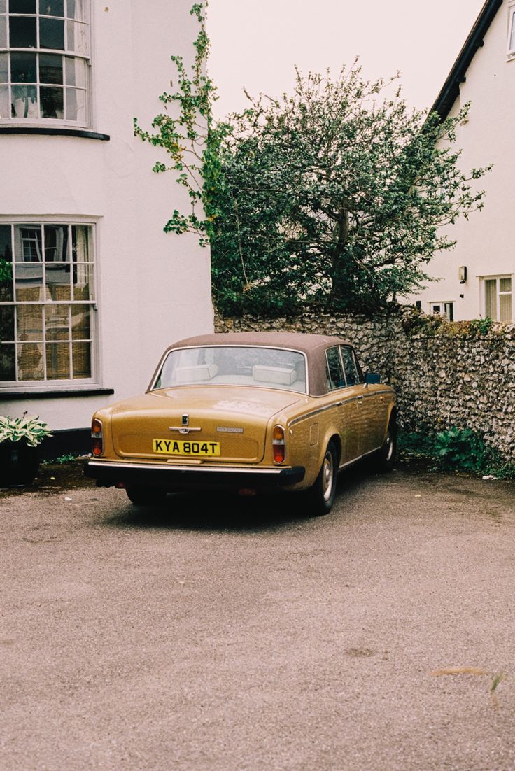 an old yellow car parked in front of a white house