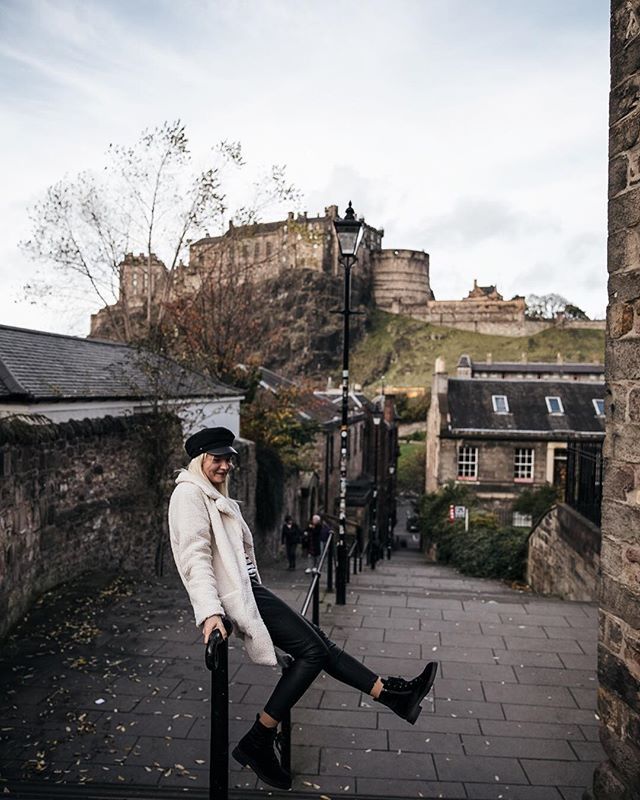 a man sitting on top of a black pole next to a stone wall and buildings