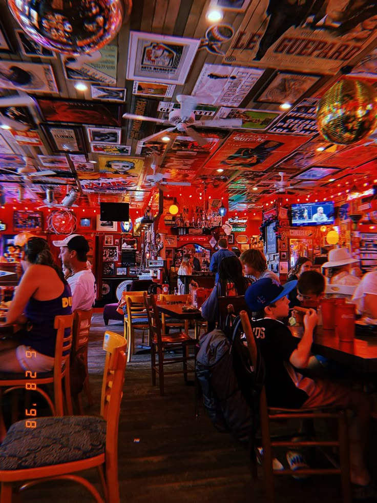 people sitting at tables in a restaurant with neon lights hanging from the ceiling above them