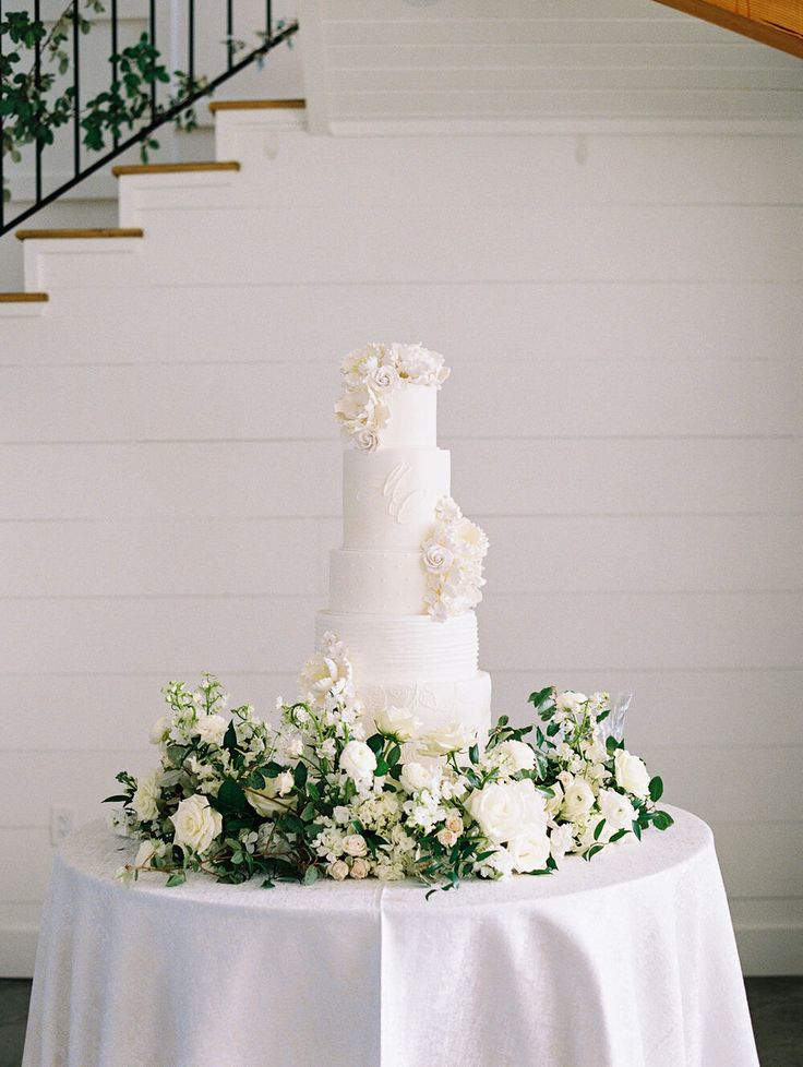 a white wedding cake sitting on top of a table next to a stair case with flowers