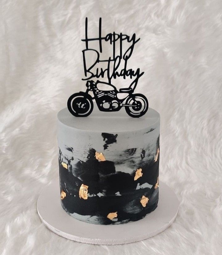 a black and white birthday cake with a motorcycle on top is sitting on a fluffy surface