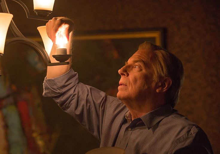 a man holding a lit candle in his hand and looking up at the ceiling light