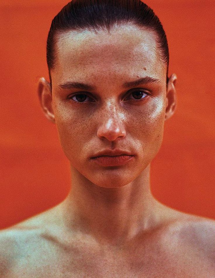 a woman with freckled hair and no shirt on posing for a photo in front of an orange wall