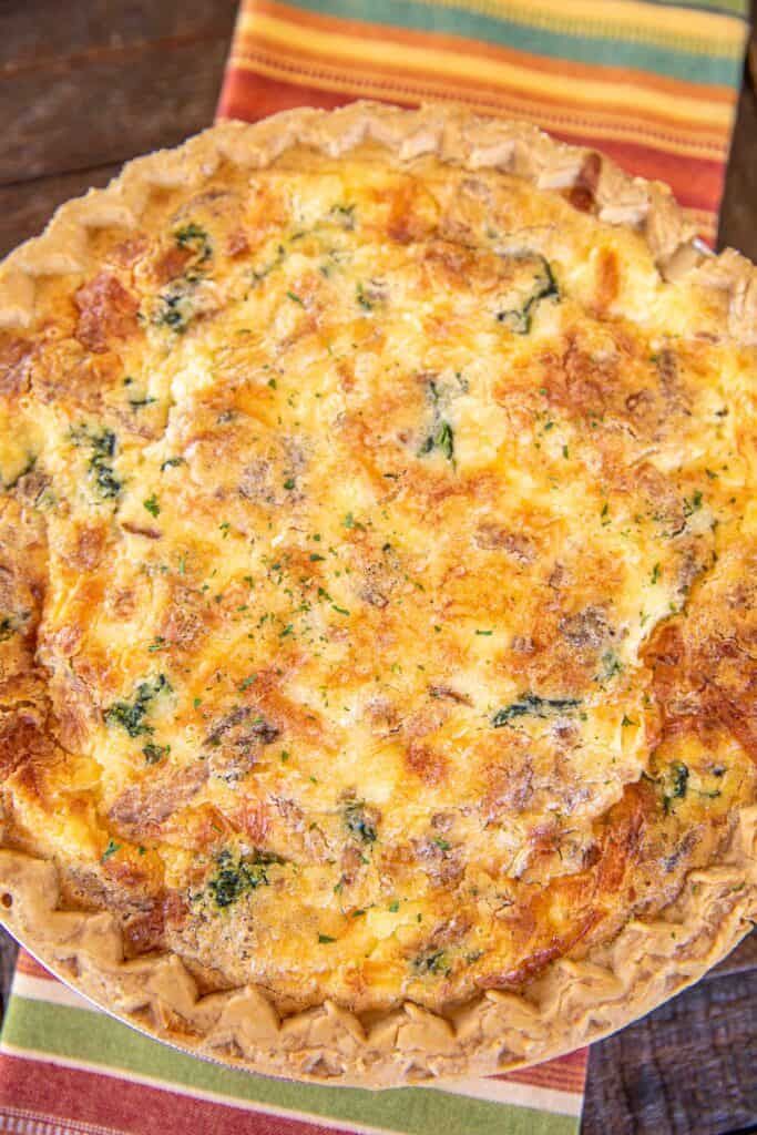 a quiche with cheese and spinach on a striped table cloth, ready to be eaten