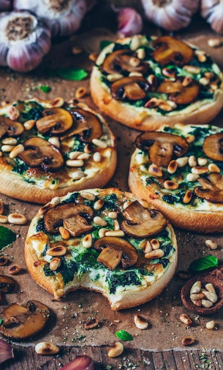 small pizzas with mushrooms, spinach and pine nuts on a wooden table next to garlic cloves