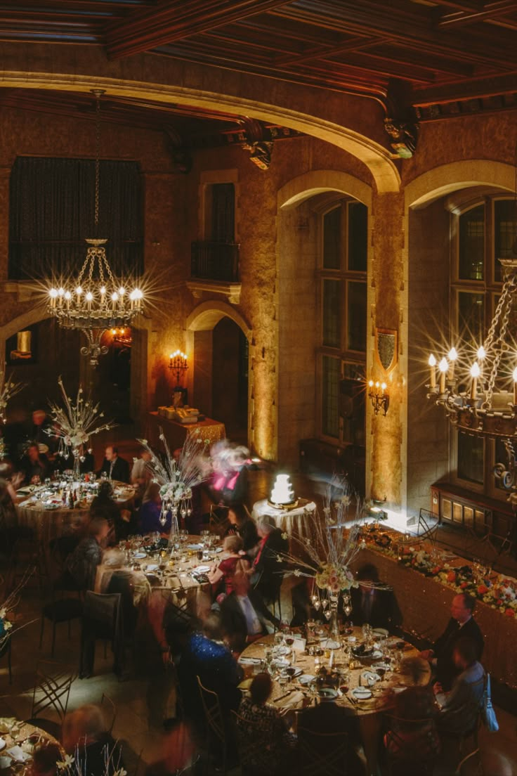 a group of people sitting at tables in a room with chandeliers hanging from the ceiling