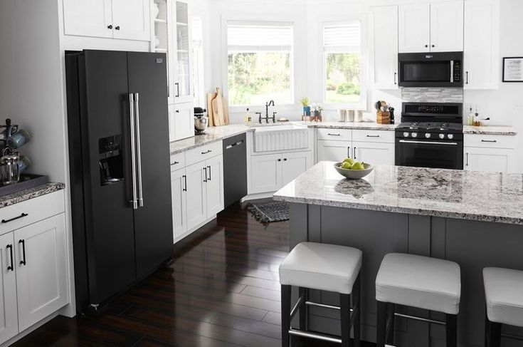 a black and white kitchen with stools next to the counter top, stove and refrigerator