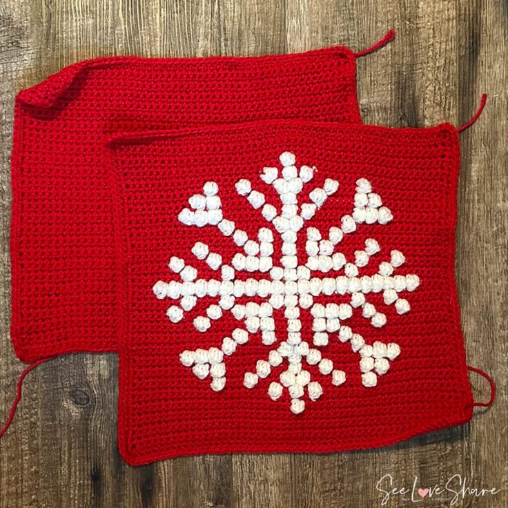 two red crocheted bags with white snowflakes on them sitting on a wooden surface