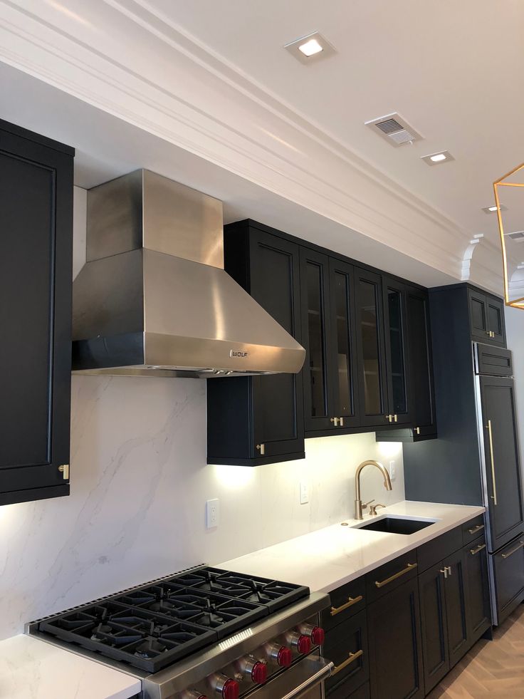 a kitchen with black cabinets and white counter tops, stainless steel range hood over the stove