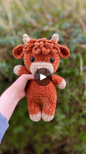 a hand holding a small stuffed animal in front of some bushes and trees with the video showing how to make an amigurt teddy bear