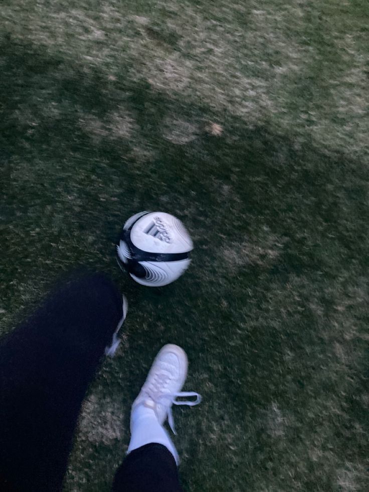 a person standing next to a soccer ball on top of a grass covered field in front of their feet