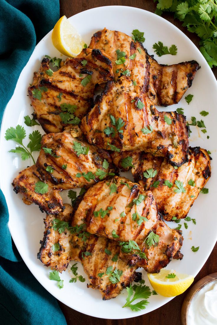 grilled chicken on a white plate with lemon wedges and cilantro