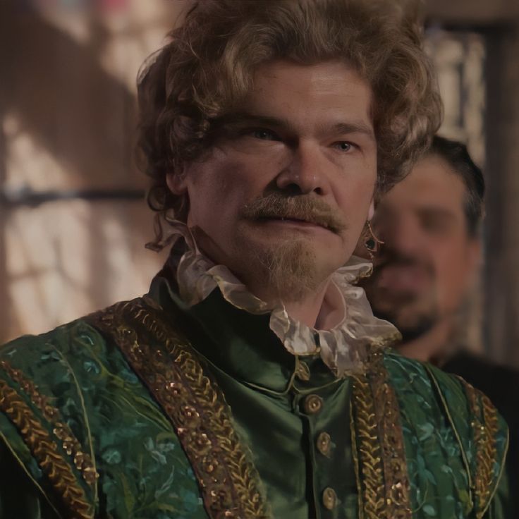 a man with curly hair wearing a green shirt and gold trimming on his face