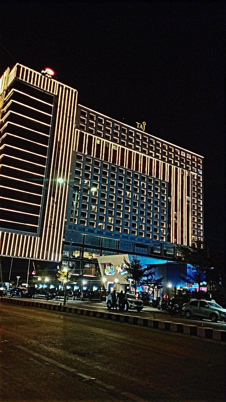 a very tall building lit up at night with cars parked in the street below it