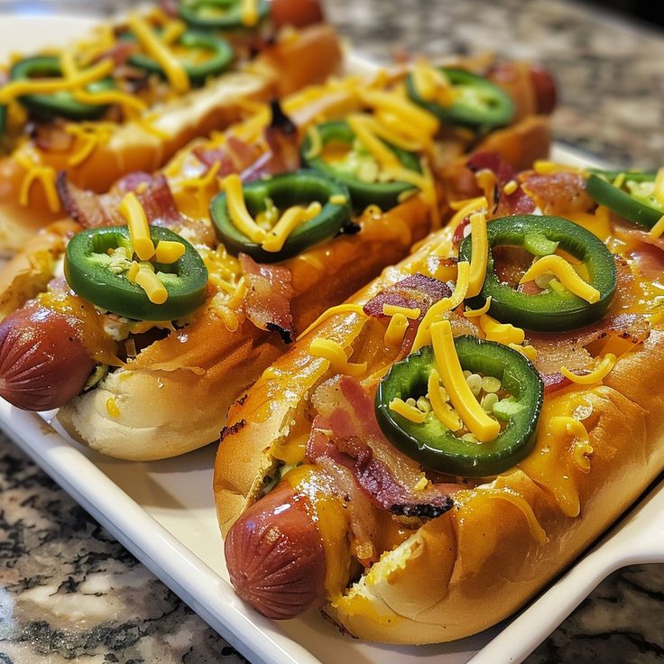 three hot dogs on buns covered in cheese and jalapenos sitting on a plate