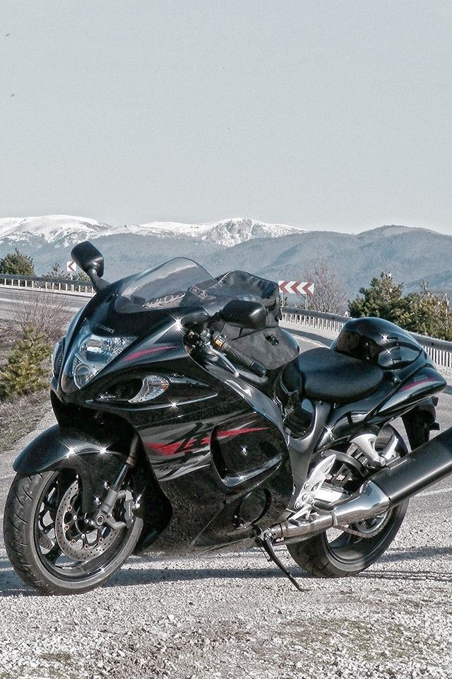 the motorcycle is parked on the side of the road near some trees and mountains in the background