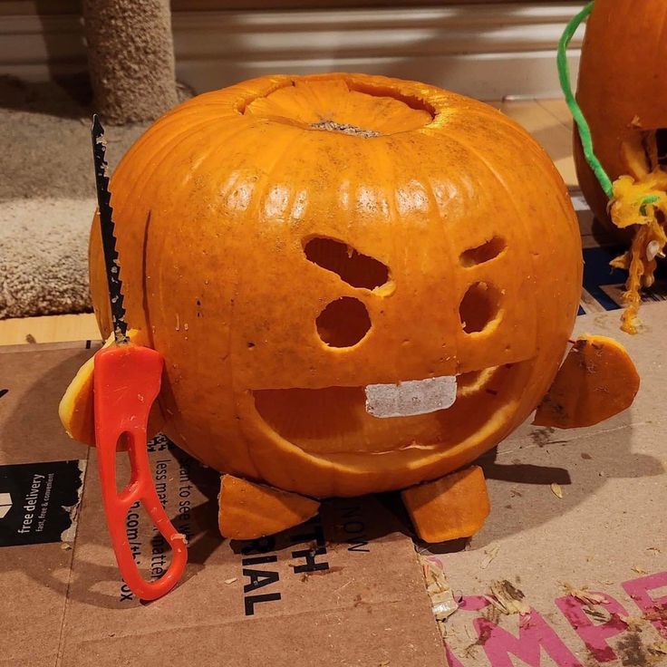 an orange pumpkin with holes in it sitting on top of a cardboard box next to a pair of scissors