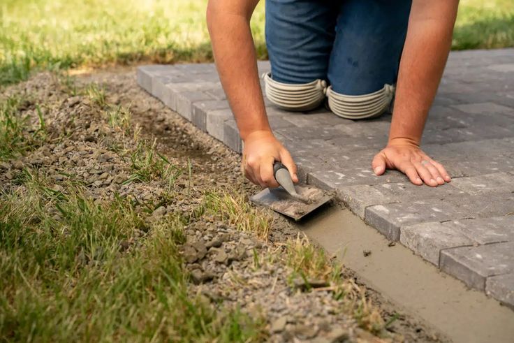 a person using a trowel to dig in the ground next to a sidewalk