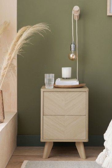 a nightstand with a candle and vase on it in front of a green painted wall