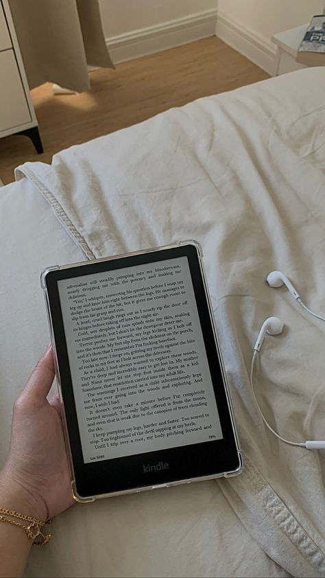 a person is holding an electronic device in their hand while sitting on a bed with headphones