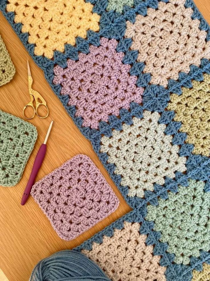 a crocheted granny blanket next to a pair of scissors and yarn on a table