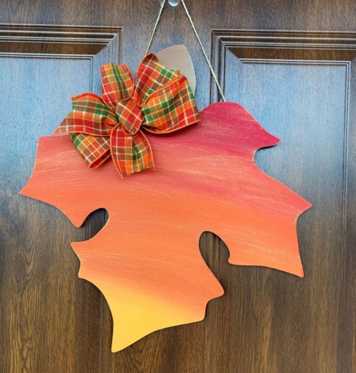 This fall leaf door hanger is the perfect decor for your front door this season. Painted in an ombre effect, we start with a deep burgundy and sweep into a burnt orange then sweep into a yellow. Finished with sweeps of metallic gold this leaf will sure look beautiful on your front door. Comes ready to hang with a seasonal plaid bow. Leaf Dimensions are 16 inch x 1/4" depthThis door hanger is made from cabinet grade MDF and is sanded, primed, painted and sealed with a clear, UV sealer to protect Leaf Door Hanger, Wood Leaves Decor, Fall Greetings, Fall Eats, Vintage Fall Decor, Pet Rock, Round Signs, Fall Door Hanger, American Flag Decor