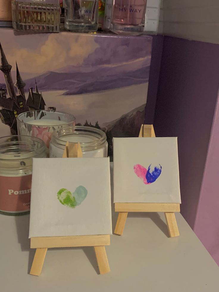 two small easels with paintings on them in front of a painting and candle holder