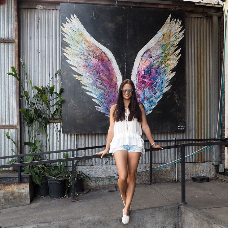 a woman standing in front of a painting with angel wings on it's back