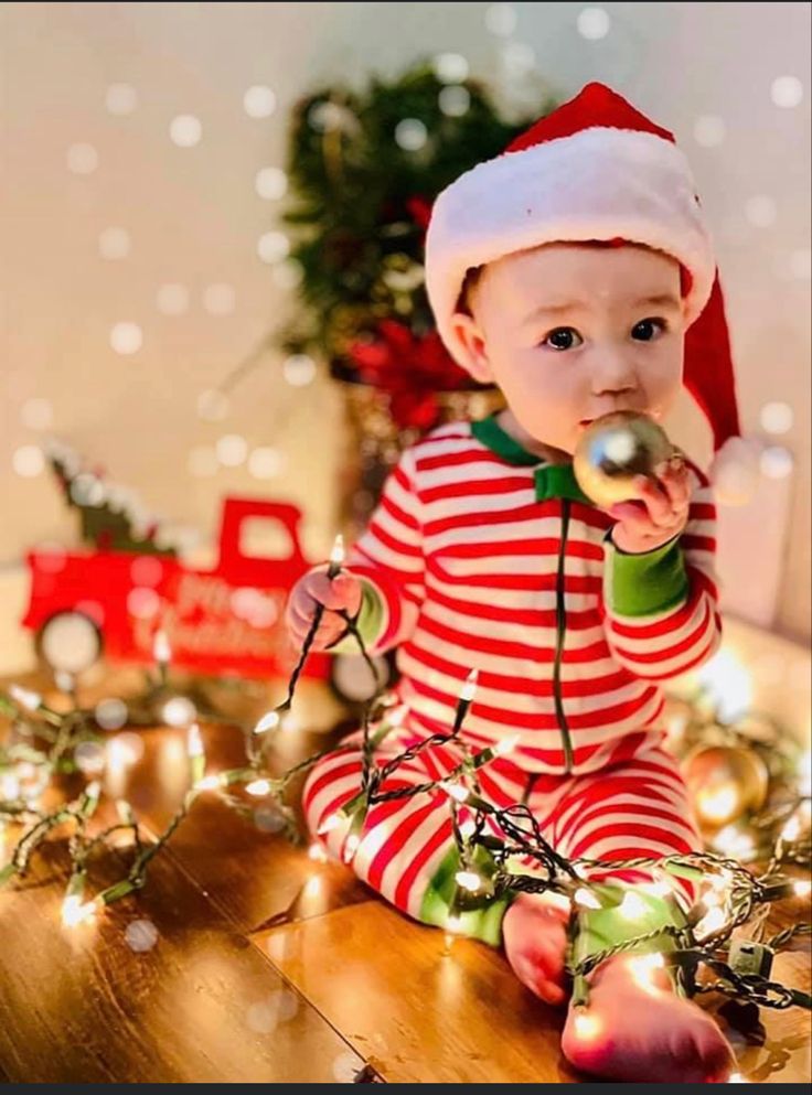 a baby sitting on the floor wearing a santa hat and holding something in its mouth