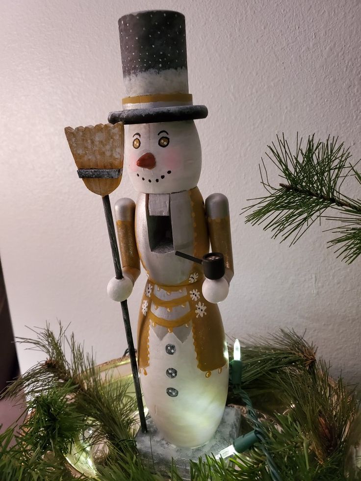 a snowman figurine holding a broom on top of a christmas tree branch