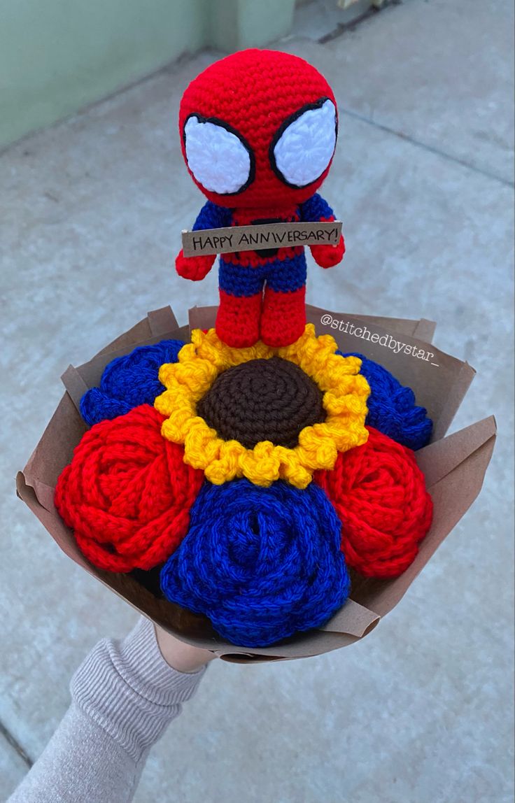 a hand holding a crocheted spiderman bouquet with flowers in it's center