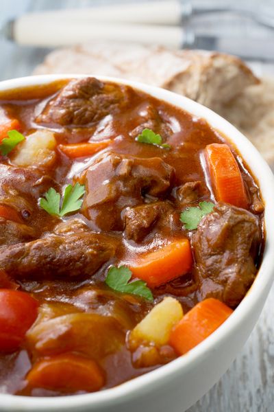 a white bowl filled with stew and carrots on top of a wooden cutting board